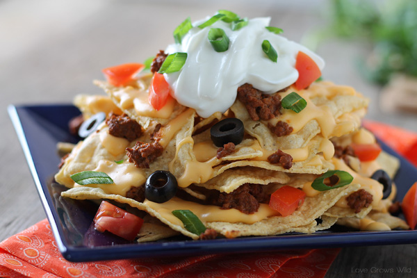 Chili Cheese Nachos are the perfect party food, with layers of beefy chili, homemade cheese sauce, and piled high with tasty toppings!