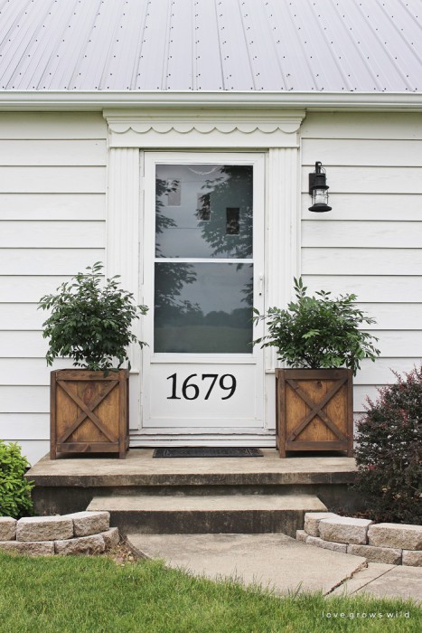 Get all the details of this charming front porch makeover featuring DIY wood planters and a lantern light fixture. | LoveGrowsWild.com