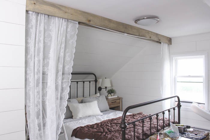 This cozy sleeping nook was created by adding a faux wood beam and lace curtains over the bed, and the results are amazing! See how to do this project in your home at LoveGrowsWild.com