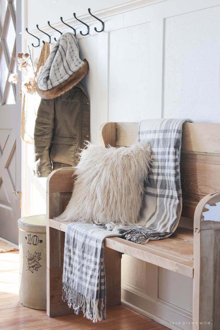 This simple farmhouse entryway is perfectly decorated for winter with large coat hooks, a rustic bench, and a place for snow-covered boots. See more photos at LoveGrowsWild.com