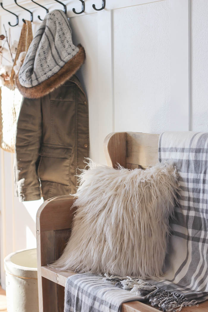 This simple farmhouse entryway is perfectly decorated for winter with large coat hooks, a rustic bench, and a place for snow-covered boots. See more photos at LoveGrowsWild.com