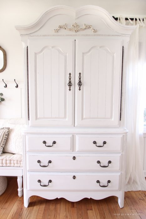 A dark and dated armoire gets a makeover with creamy white paint and beautifully distressed details. Find out how to easily antique furniture with this tutorial!