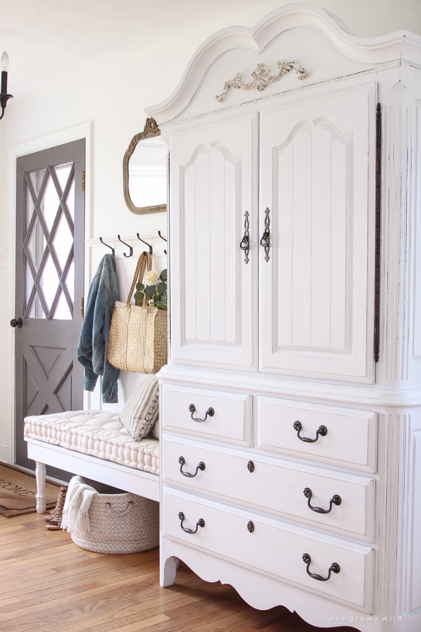 A dark and dated armoire gets a makeover with creamy white paint and beautifully distressed details. Find out how to easily antique furniture with this tutorial!