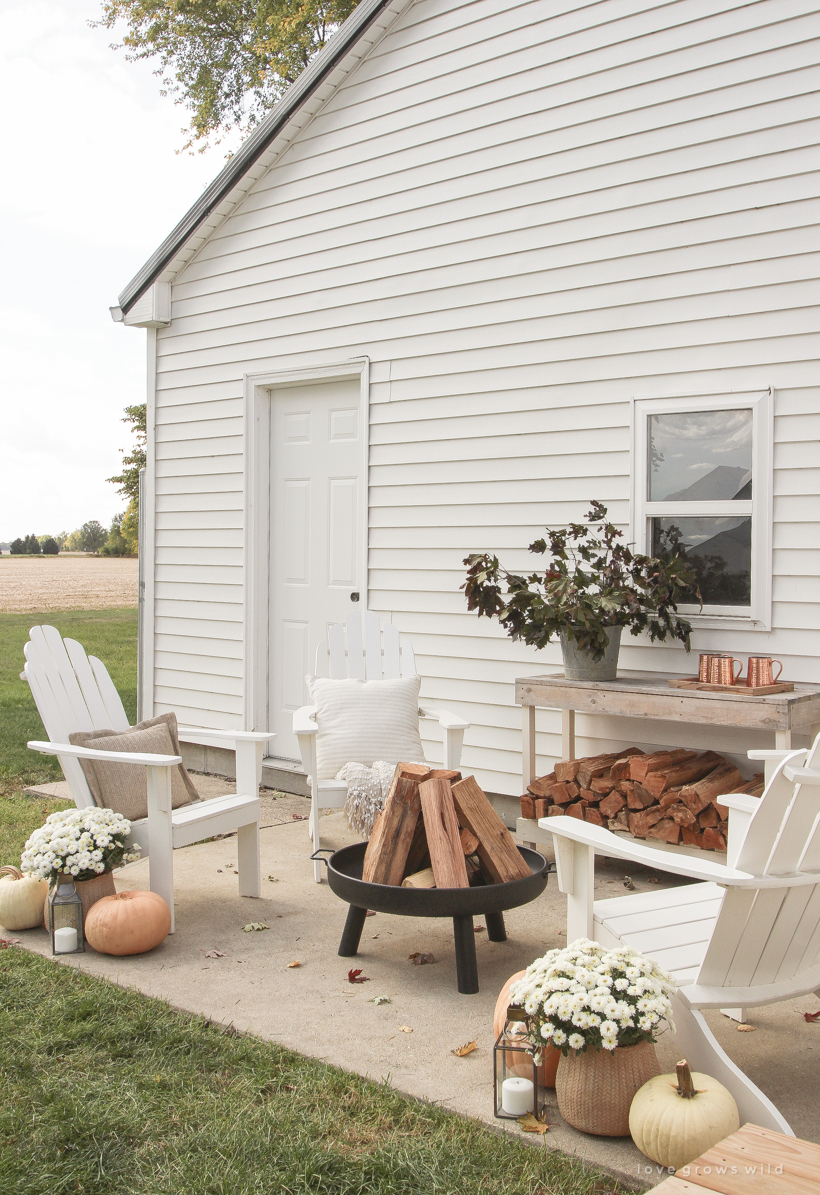 A cozy outdoor space to relax in with a simple fire pit, white adirondack chairs, and beautiful fall decor. See more details at lovegrowswild.com