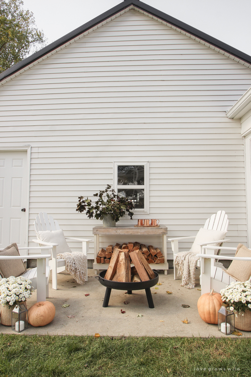 A cozy outdoor space to relax in with a simple fire pit, white adirondack chairs, and beautiful fall decor. See more details at lovegrowswild.com